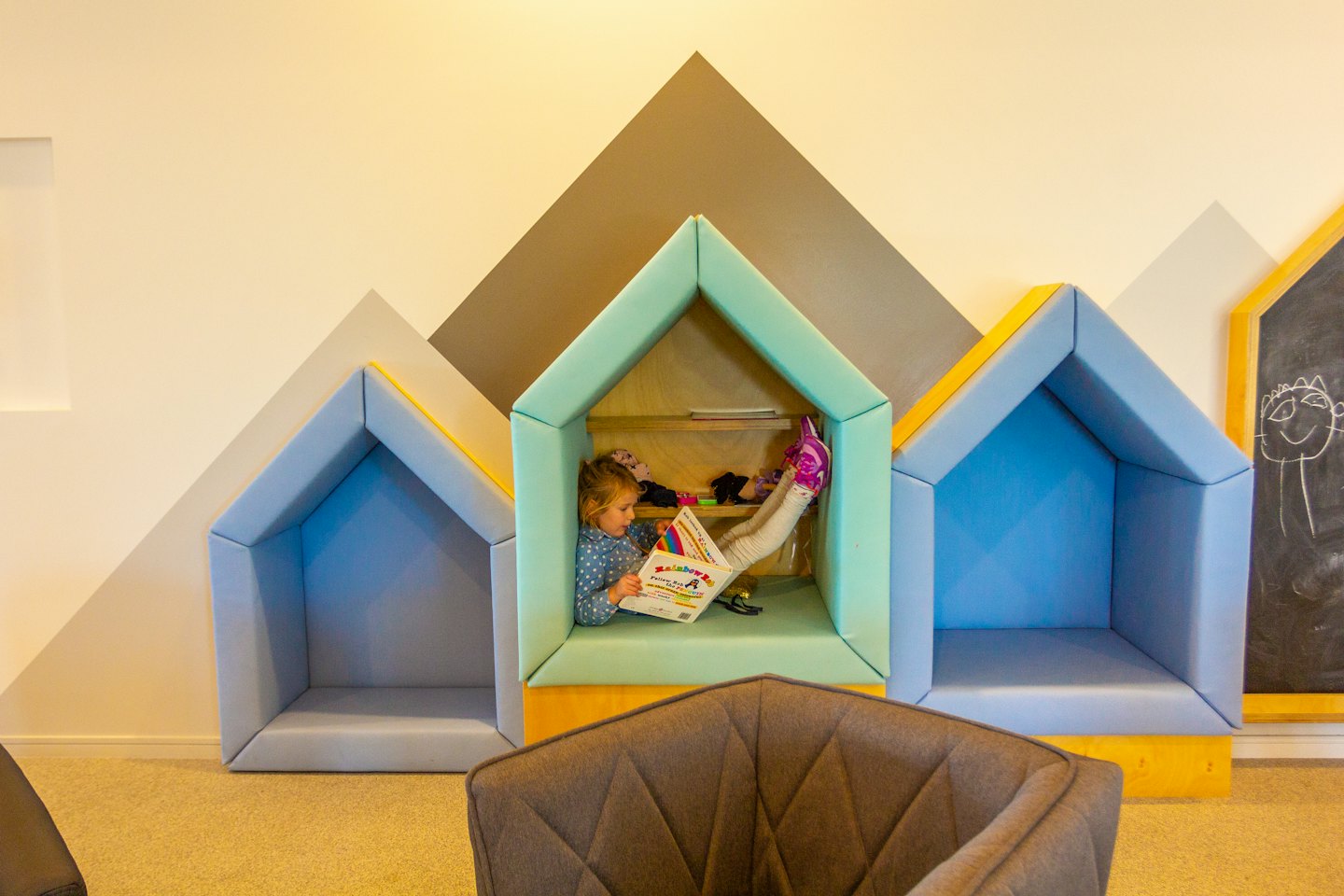 Child reading a colorful book inside a house-shaped wall nook.