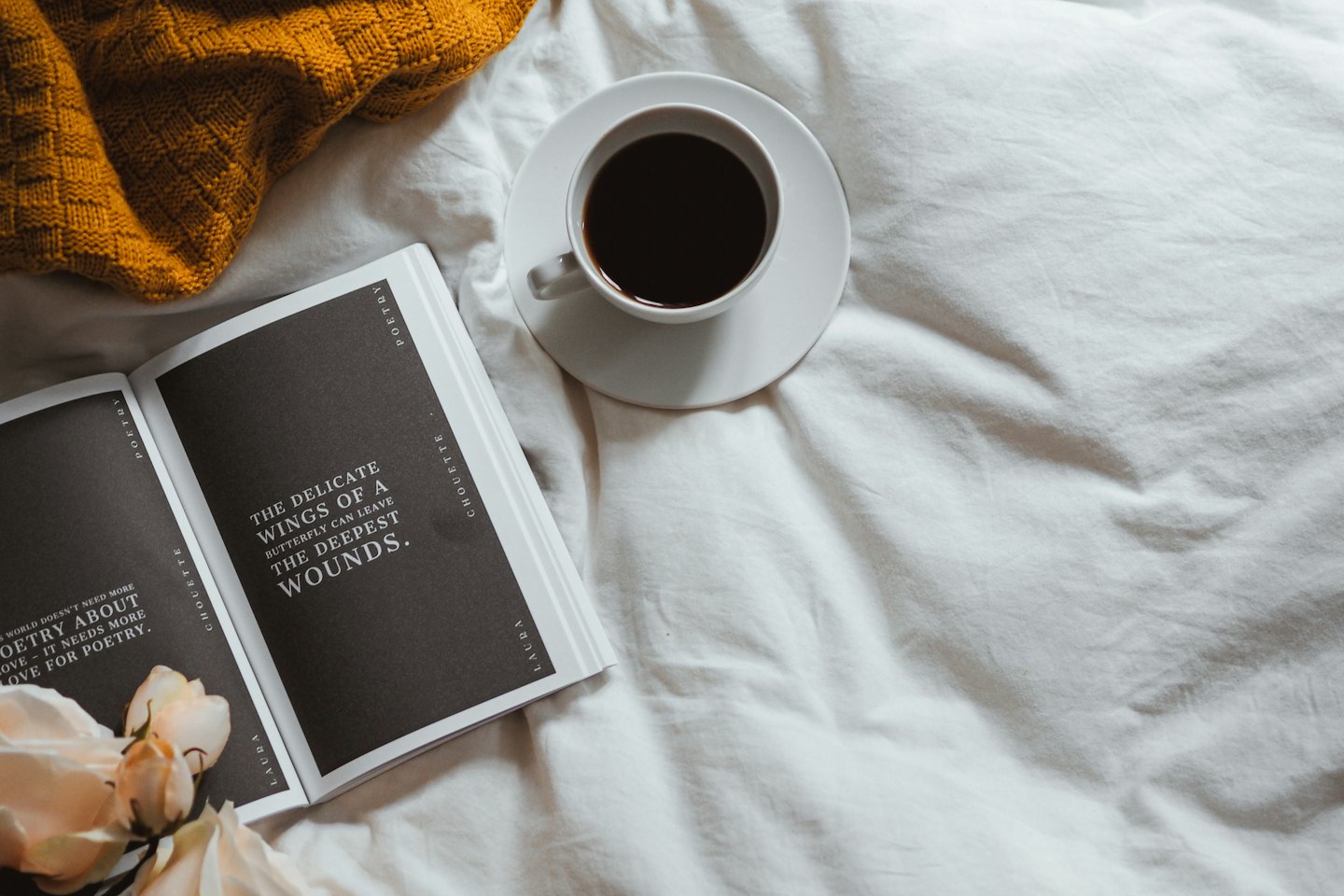 Open poetry book and coffee cup resting on white sheets.